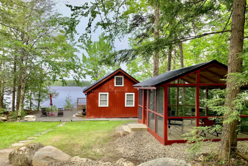 A red cabin and a screened porch surrounded by trees, overlooking a serene lake.