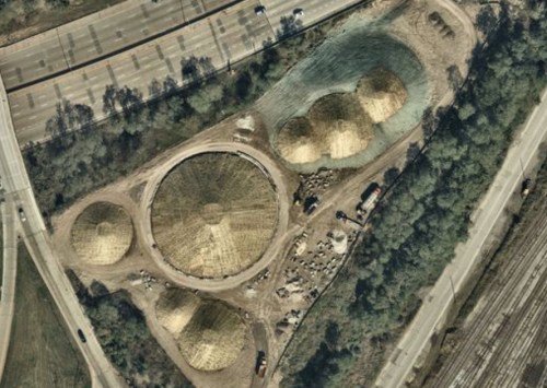Aerial view of large circular structures surrounded by trees and roads, with several smaller mounds nearby.