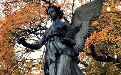 A bronze angel statue surrounded by vibrant autumn foliage.