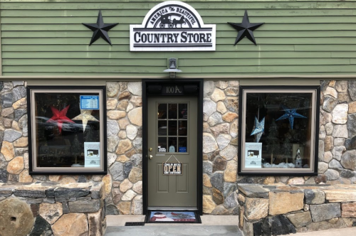 A rustic country store with a stone facade, green siding, and star decorations in the windows. The door is open.