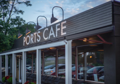 Exterior of Ports Cafe with large windows, outdoor seating, and a cloudy sky in the background.