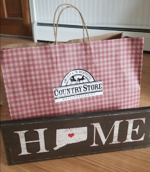 A checkered bag from a country store next to a wooden sign that reads "HOME" with a heart over the state of Connecticut.