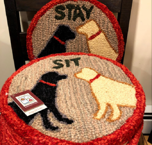 Two round rugs featuring a black dog and a yellow dog, labeled "STAY" and "SIT," on a wooden chair.