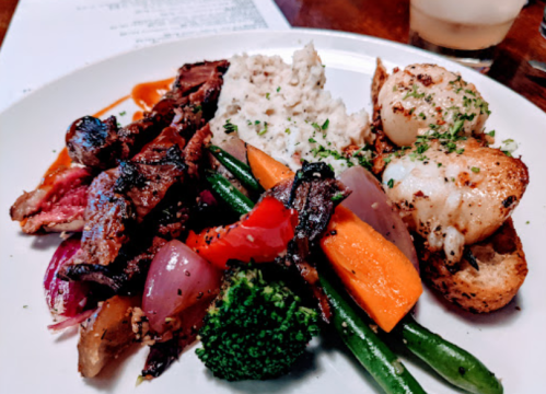 A plate of grilled meats, sautéed vegetables, rice, and garnishes, showcasing a colorful and appetizing meal.