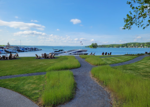 A scenic view of a lake with boats, surrounded by green grass and pathways under a clear blue sky.