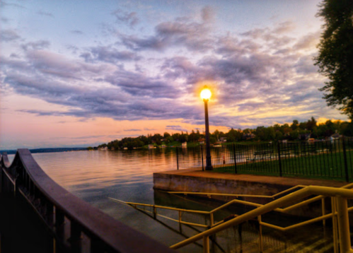 A serene lakeside view at sunset, with clouds reflecting on the water and a lamppost illuminating the scene.