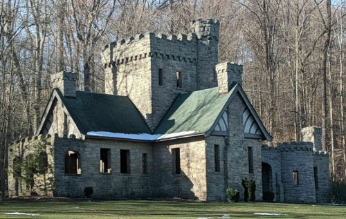 A stone castle with turrets, surrounded by trees and a patch of snow on the ground.
