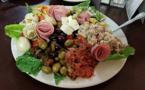 A colorful platter featuring assorted meats, cheeses, olives, vegetables, and dips on a bed of lettuce.