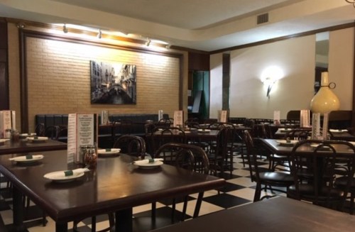 A spacious restaurant with wooden tables, chairs, and a brick wall, featuring a large painting and menus on each table.