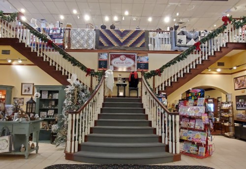 A festive staircase in a gift shop, decorated with garlands and quilts, leading to a cozy display area.
