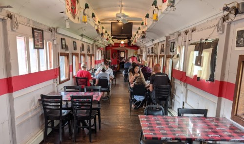 Interior of a dining car with tables, chairs, and patrons enjoying their meals in a cozy, vintage setting.