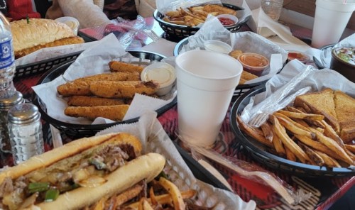 A table filled with various food items, including sandwiches, fries, and dipping sauces in baskets and cups.