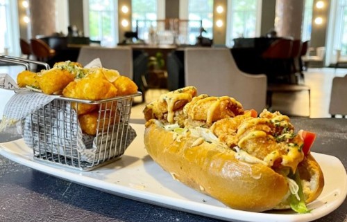 A plate featuring a loaded seafood sandwich and a side of crispy tater tots in a small basket.
