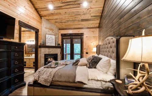 Cozy bedroom with wooden walls, a plush bed, fireplace, and stylish decor, creating a warm, inviting atmosphere.