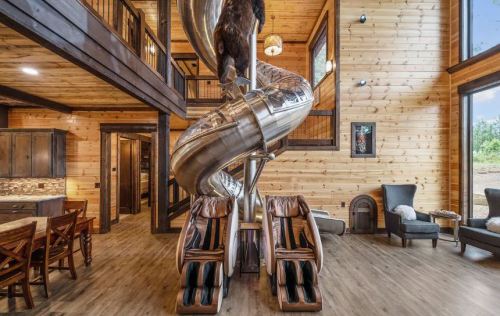A modern wooden interior featuring a large slide, massage chairs, and a bear sculpture, creating a playful atmosphere.