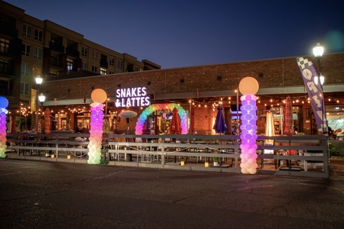 Exterior of Snakes & Lattes at night, featuring colorful balloon decorations and string lights.