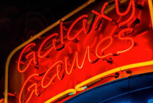 Neon sign reading "Galaxy Games" in bright red and yellow lights against a dark background.