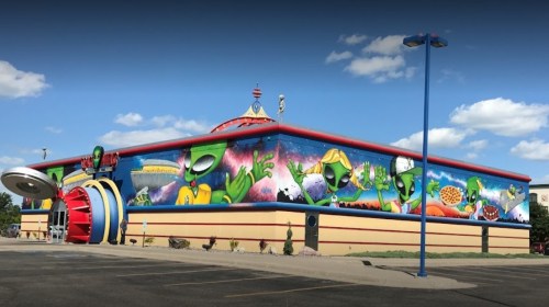 Colorful alien-themed mural on a building, featuring cartoon aliens and a whimsical design against a blue sky.
