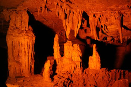 Stalactites and stalagmites illuminated in warm orange light inside a cave.
