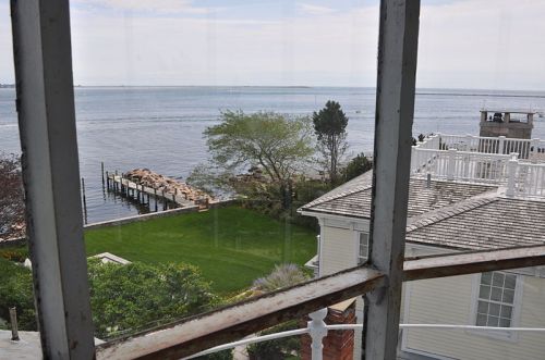 View from a window overlooking a calm waterfront, with a green lawn and a dock extending into the water.