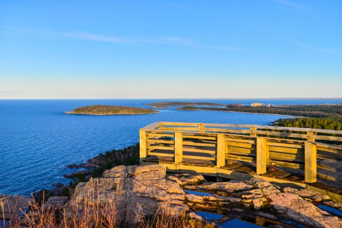 A wooden overlook with a view of a calm blue sea and distant islands under a clear sky.