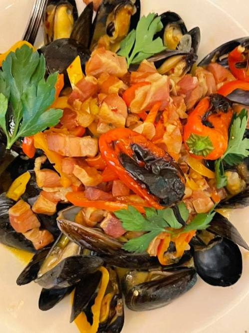 A plate of mussels topped with diced bacon, bell peppers, and fresh parsley.
