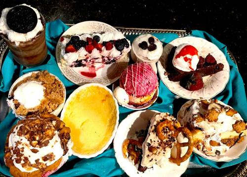 A variety of desserts on a tray, including ice cream, cakes, and fruit toppings, all with whipped cream and garnishes.