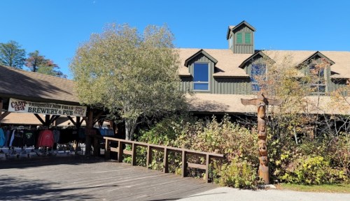 A rustic brewery and pub building with a wooden deck, surrounded by trees and autumn foliage.