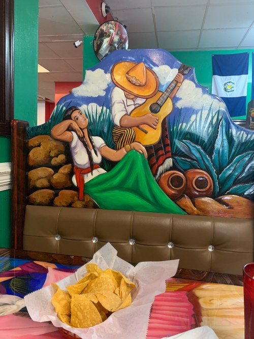 A colorful mural of a musician playing guitar and a woman in traditional attire, with a plate of chips in the foreground.