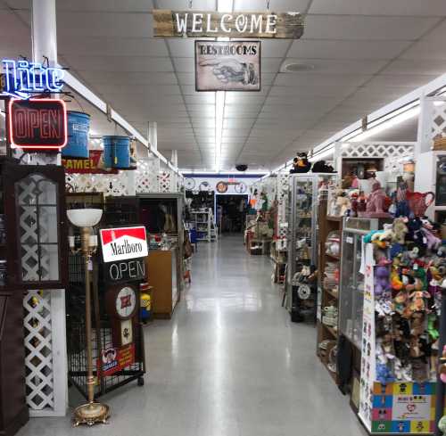 A wide aisle in a vintage shop filled with various items, signs, and decorations, with a "Welcome" sign overhead.