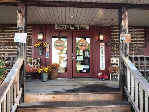 A welcoming storefront with double doors, fall decorations, and signs saying "Bless All Who Enter" and "Happy Fall."