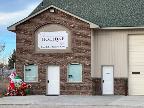 A brick building with a sign reading "The Holidae Shop," featuring holiday decorations outside.