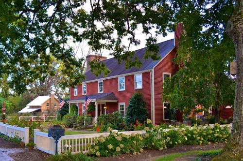 A charming red house with white trim, surrounded by greenery and flowers, featuring American flags on the porch.