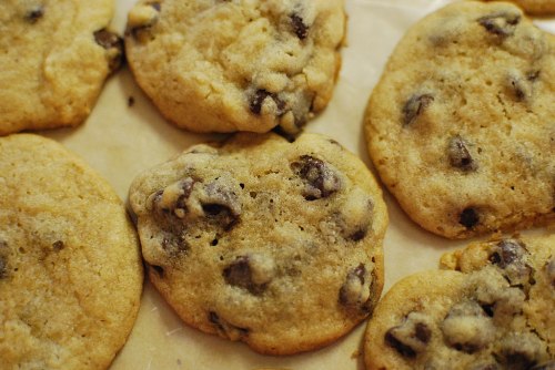 Freshly baked chocolate chip cookies on parchment paper, golden brown with melted chocolate chips.