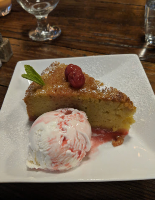 A slice of cake topped with a raspberry sauce and a scoop of ice cream, garnished with a mint leaf on a white plate.