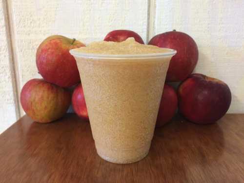 A cup filled with a brown substance, surrounded by red and green apples on a wooden surface.