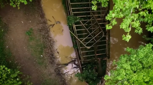 Aerial view of a rusted structure partially submerged in muddy water, surrounded by lush green trees.