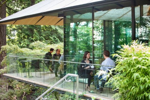 A modern glass building in a lush garden, with people sitting and chatting on a balcony.