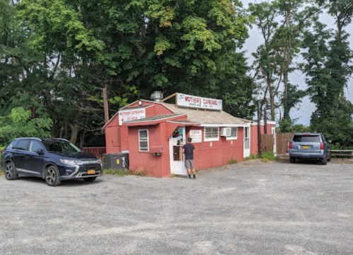 A small red building labeled "Mother's Cupboard" with cars parked outside and a person at the window.