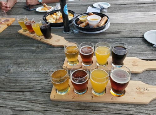 A wooden flight board with various craft beer samples and snacks on a rustic table.