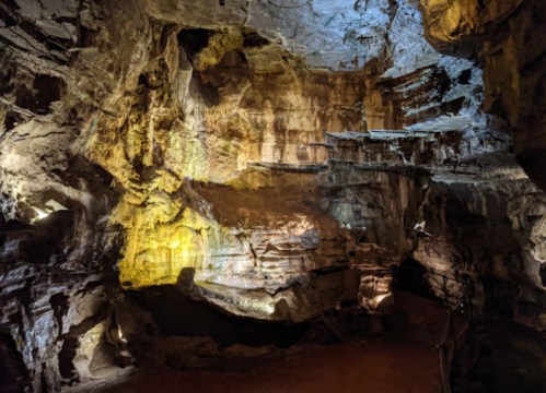 A dimly lit cave with textured rock formations and illuminated areas, showcasing natural geological features.
