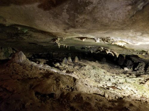 A dimly lit cave interior with rocky formations and stalactites hanging from the ceiling.