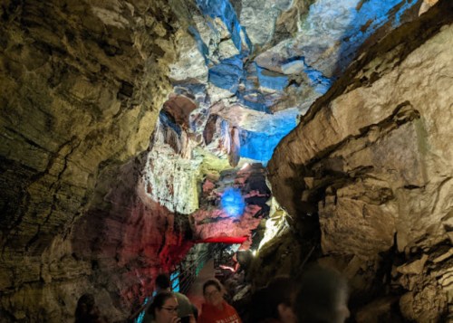 A colorful cave interior with illuminated rock formations and visitors exploring the space.