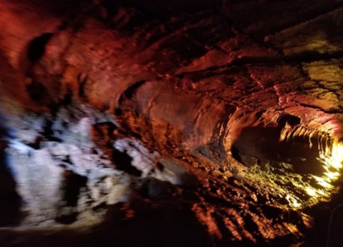 A dimly lit cave with red and orange rock formations, showcasing textured walls and shadows.