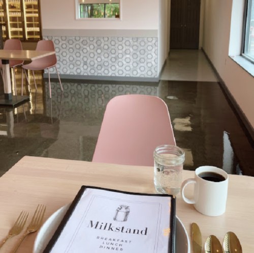 A cozy café setting with a menu on a table, a cup of coffee, and a glass of water, featuring pink chairs and modern decor.