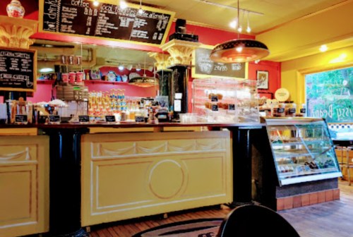 A colorful café interior featuring a counter with coffee options, a display case, and vibrant wall decor.