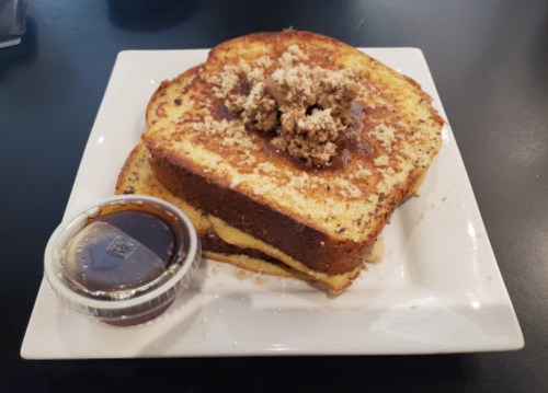 A plate of French toast topped with crumbled topping and served with a side of syrup.