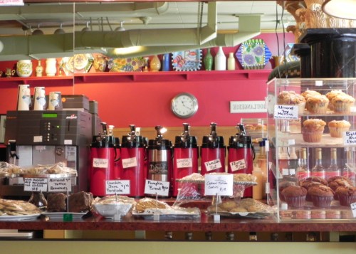 A café display featuring coffee dispensers, baked goods, and muffins in a colorful setting.