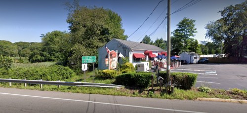 A roadside view of a restaurant with outdoor seating, surrounded by greenery and a parking lot.