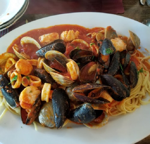 A large plate of seafood pasta with shrimp, mussels, clams, and a rich tomato sauce over spaghetti.